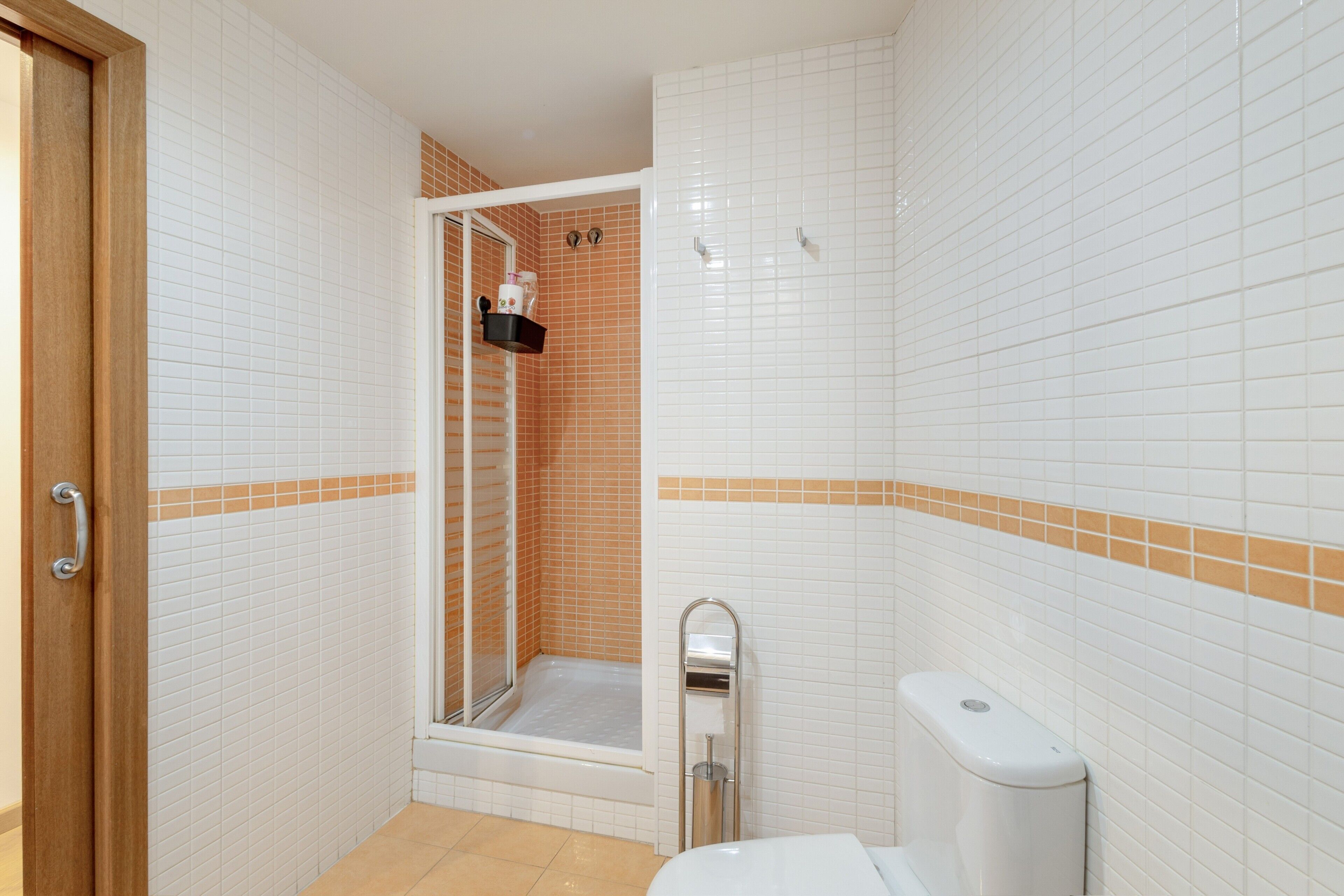 Een badkamer met witte betegelde wanden, een douchegedeelte, een toilet en een deur.