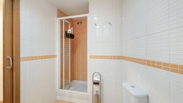 Een badkamer met witte betegelde wanden, een douchegedeelte, een toilet en een deur.