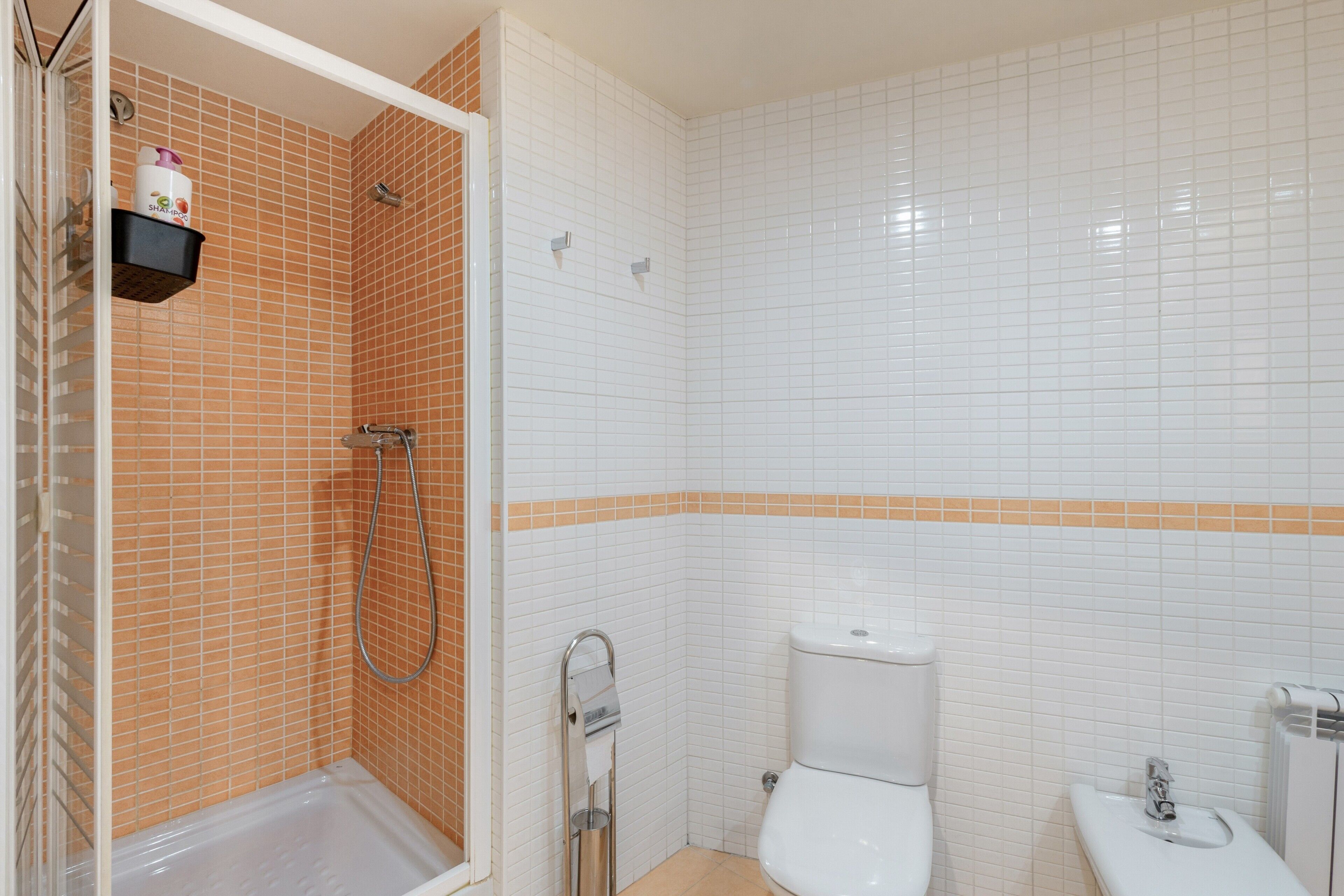 A bathroom with a shower, toilet, and sink, featuring white and orange tiles.