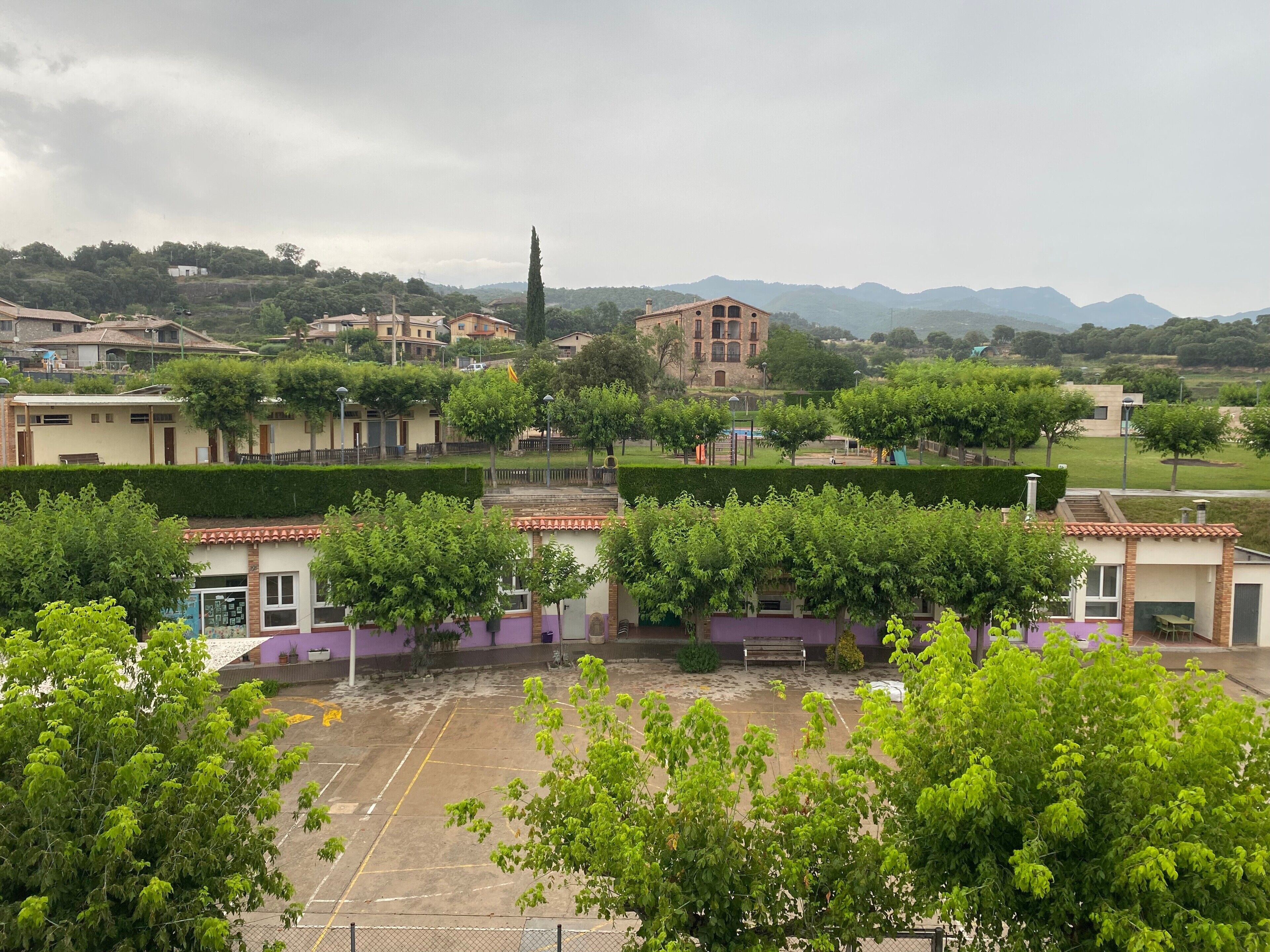 A courtyard with a tennis court, surrounded by buildings with traditional architecture, and a view of distant mountains.