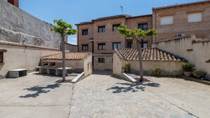 Un patio con suelo de piedra, un edificio con tejado de azulejos y plantas en macetas.