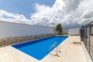 A swimming pool with a stone wall and metal railings, surrounded by a tiled deck.