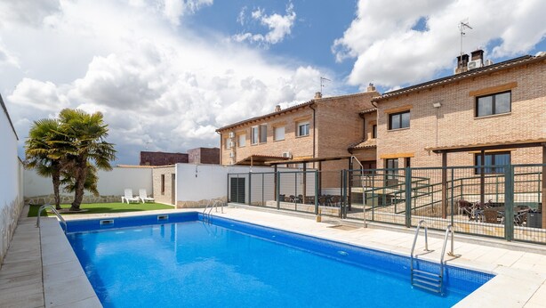 Una piscina con agua cristalina y azul, rodeada por un patio amurallado con mobiliario exterior.