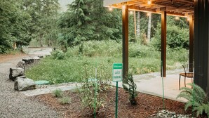 Un espace de stationnement réservé aux visiteurs, indiqué par un panneau, entouré d’une végétation luxuriante et agrémenté d’une structure en forme de pergola en bois.