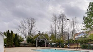 Une piscine dotée d’un kiosque, entourée d’arbres et d’une clôture.
