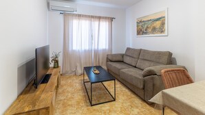 Un salon avec un canapé, un téléviseur, une table basse et un tableau accroché au mur.