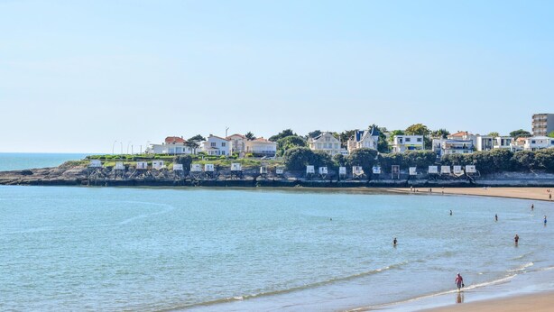 A coastal beach with a row of white houses, some with red roofs, and a sandy beach with a few people. - Nice home in Royan with WiFi (Royan)