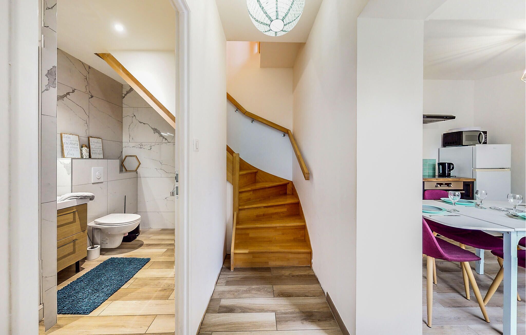 Une cuisine moderne avec un coin repas, un escalier en bois et une salle de bain équipée de toilettes et d’un lavabo.