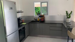 Een moderne keuken met een inbouwkoelkast, fornuis en spoelbak. Er is een raam met uitzicht op groen.