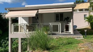 Een twee verdiepingen tellend huis met een balkon, een overdekte veranda en een kleine tuin.