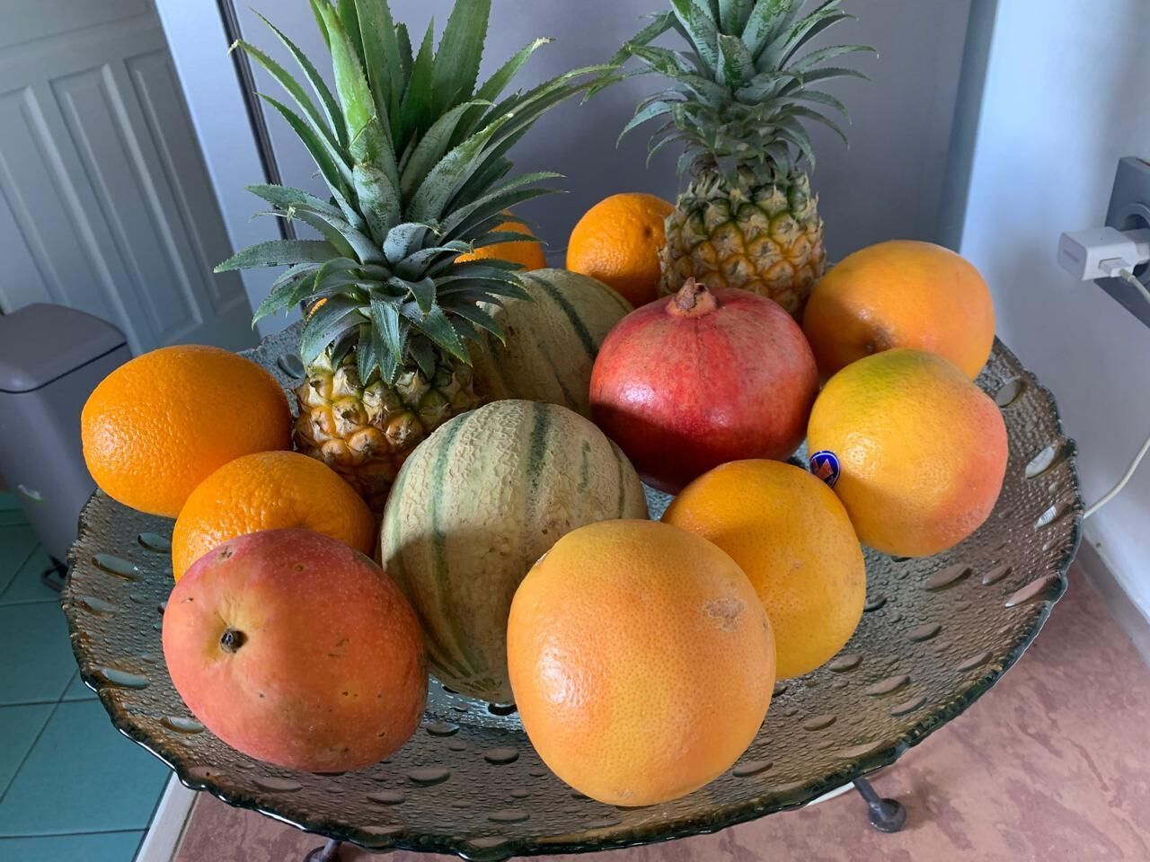 A fruit basket with various fruits including oranges, a pineapple, a pomegranate, and a mango.