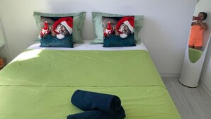 Een bed met groene beddengoed, twee kussens met een kat en kerstman ontwerp, en een blauwe handdoek op het bed.