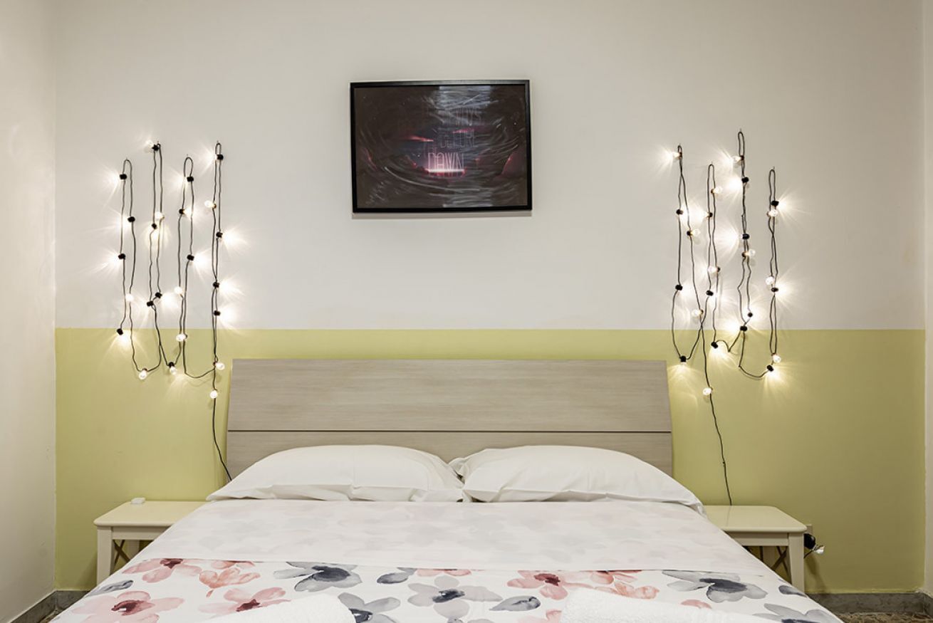 A bedroom with a bed, two bedside tables, a wall-mounted picture, and string lights.