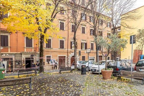 A cobblestone street with parked cars, a bench, and trees with yellow leaves.