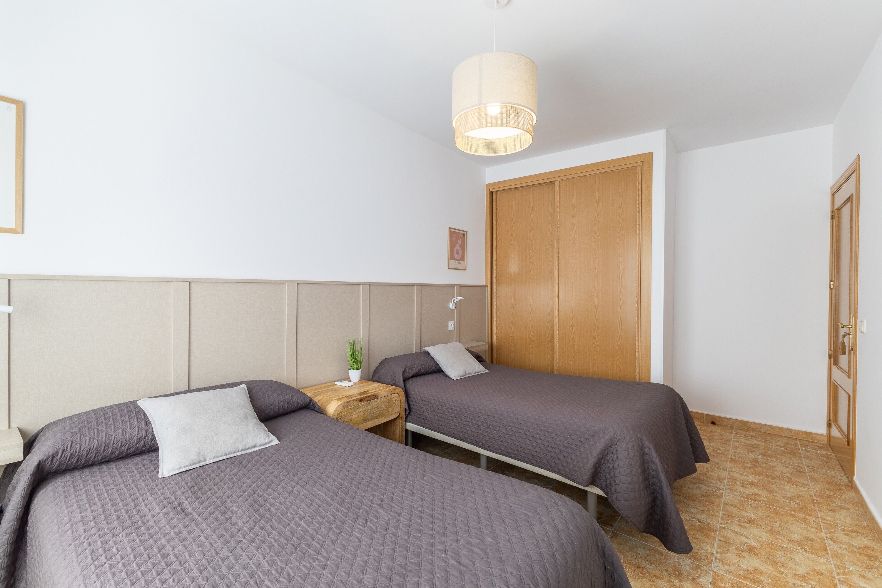 Ein Schlafzimmer mit zwei Betten, einem Holzschrank, einem Nachttisch mit Lampe und einer Hängeleuchte.