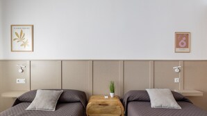 A hotel room with two beds, a wooden nightstand between them, a small potted plant, and two framed pictures on the wall.