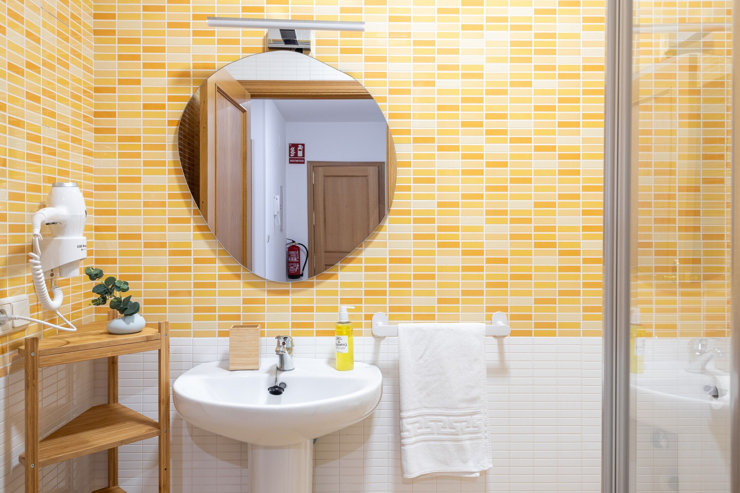 Een badkamer met gele wandtegels, een wit wastafelmeubel, een spiegel en een douche.