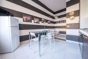 Una cocina moderna con refrigerador, una mesa de comedor de vidrio y sillas, y paredes a rayas con obras de arte.