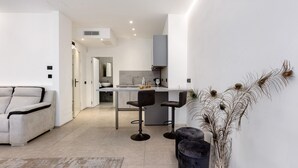 A modern interior with a sofa, two bar stools, a kitchen area, and a decorative plant.