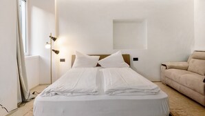 A hotel room with a bed, a lamp, a window, and a sofa.