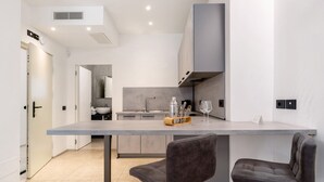 A modern kitchen with a central island, two bar stools, and a visible door leading to another room.