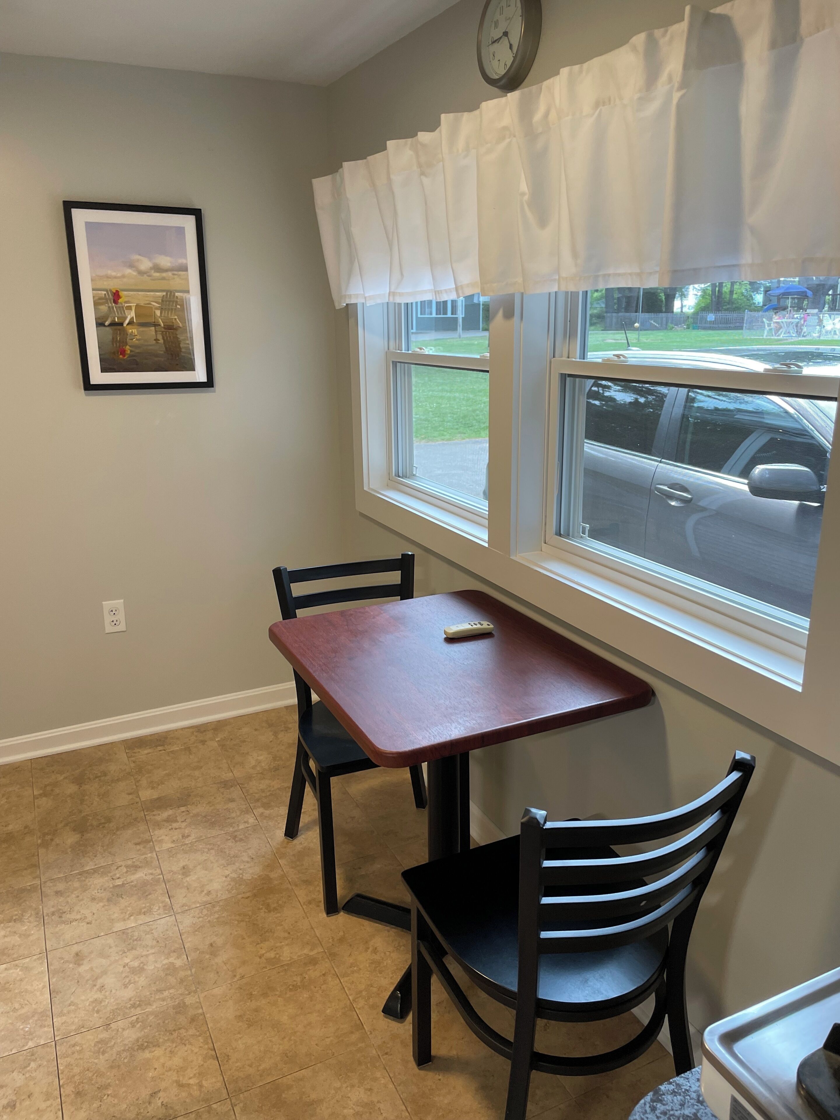 A dining area with a table and chairs, a clock on the wall, and a window with a view of the street.