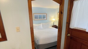 A bedroom with a bed, a nightstand, a lamp, and a door with a window. - Elmwood Motor Court (Old Orchard Beach)