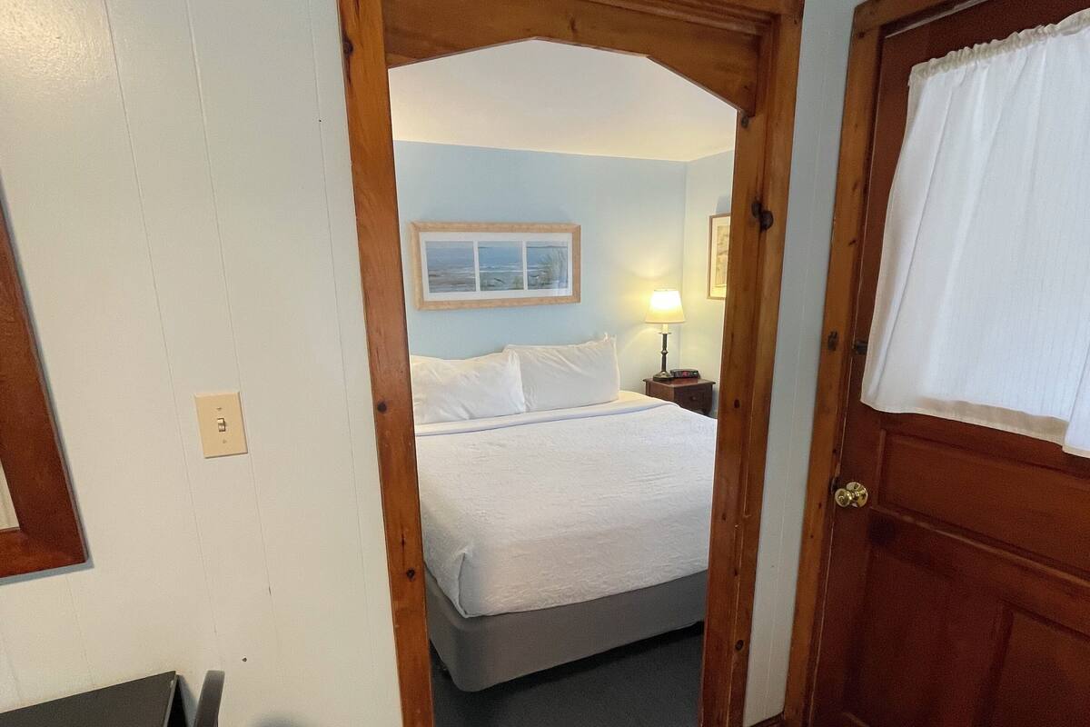 A bedroom with a bed, a nightstand, a lamp, and a door with a window.