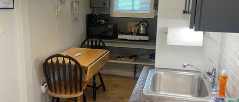 A compact kitchen with a dining table, chairs, a sink, and a stove.