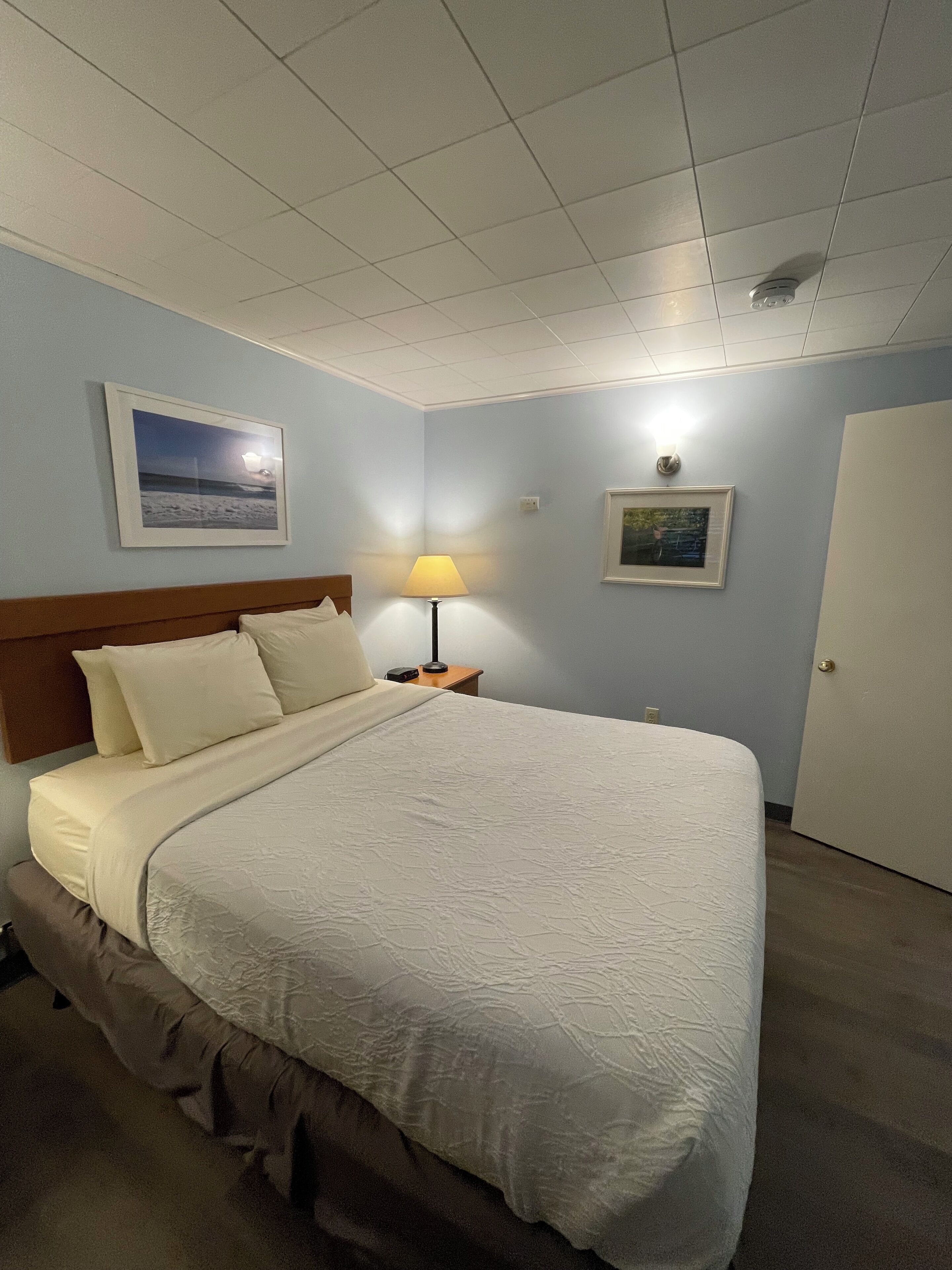 A neatly made bed with a headboard, a bedside lamp, and two framed pictures on the wall.