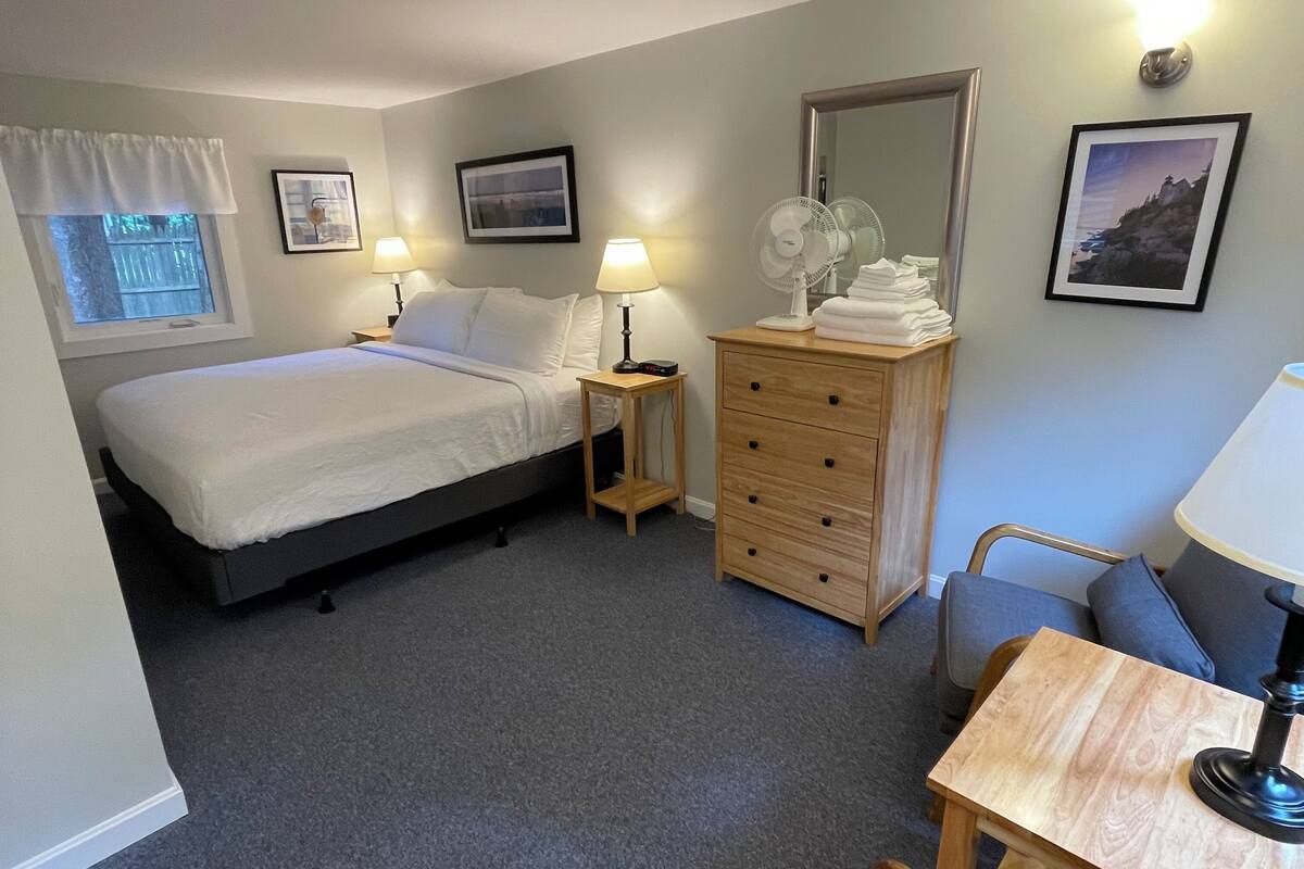 A hotel room with two beds, a wooden dresser, a desk with a chair, and a small table with a lamp.