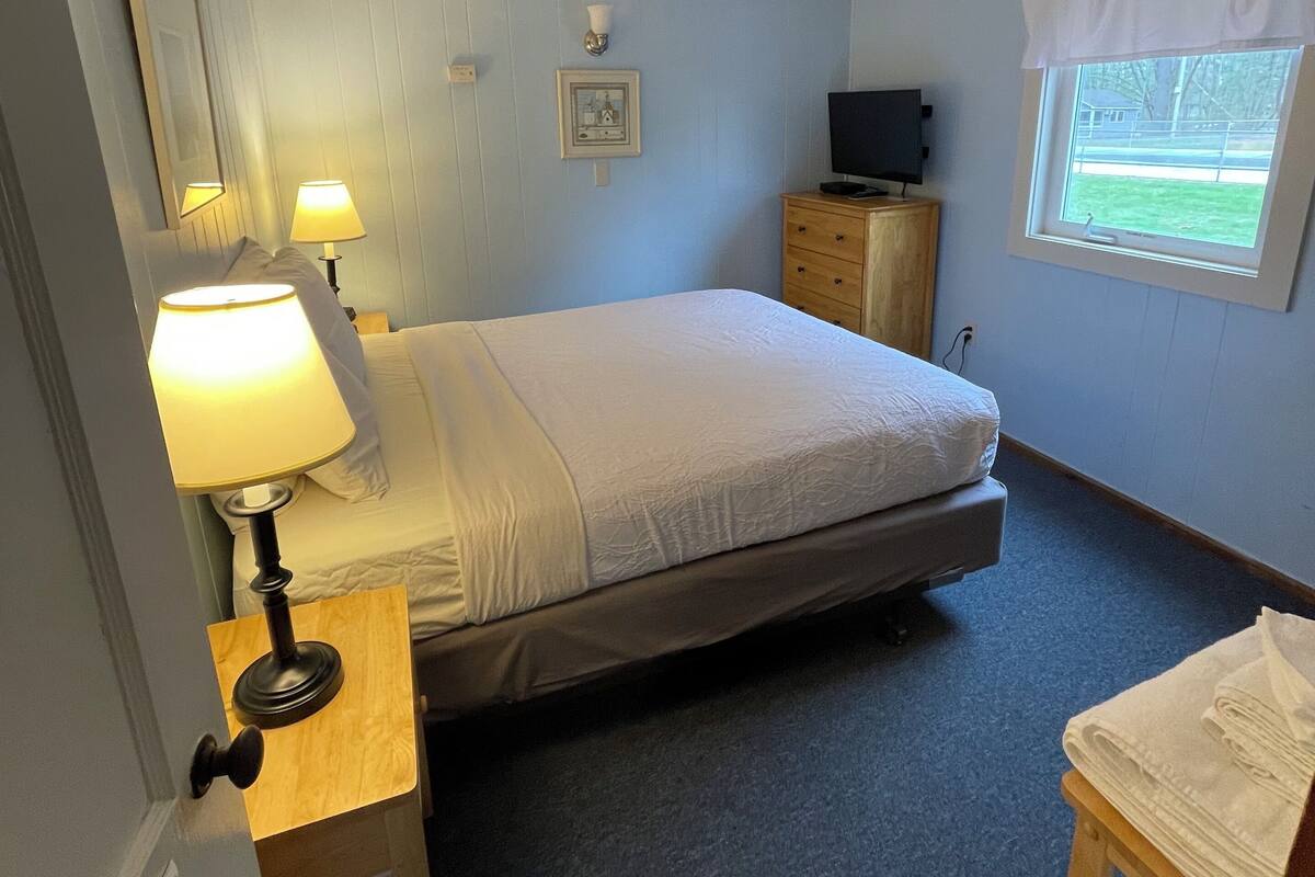 A bedroom with a bed, bedside lamps, a dresser, a television, and a window.