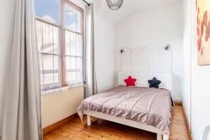 Una camera da letto con un letto, una finestra, un termosifone e una parete con un pannello bianco.