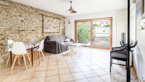 A room with a stone wall, a dining table with chairs, a sofa, a small table, a black chair, and a large sliding glass door.