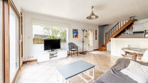 A spacious living area with a TV, seating, a staircase, and a dining area.