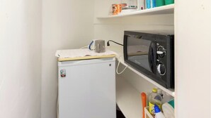 Een compacte kitchenette met een kleine koelkast, magnetron en planken met diverse spullen.