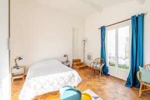 Une chambre à coucher avec un lit, une chaise, une table de chevet et une fenêtre avec des rideaux.