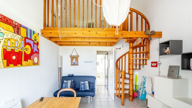 Ein modernes Interieur mit einem Holzesstisch, blauem Sofa, einer Treppe und farbenfroher Kunst.