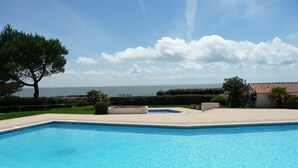 Una piscina con vistas al mar, rodeada de vegetación y un edificio con tejado de tejas.
