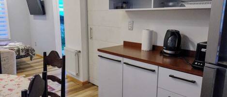 Una cocina compacta con armarios blancos, encimera de madera y cafetera integrada.