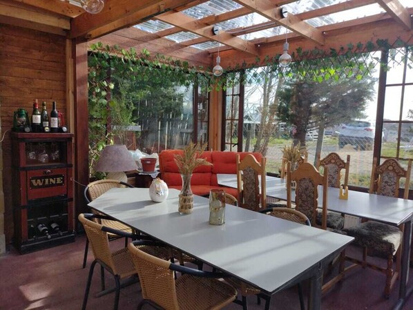 An indoor dining area with a long table, wicker chairs, a red sofa, and a wine display cabinet. - Tribal house (Punta Arenas)