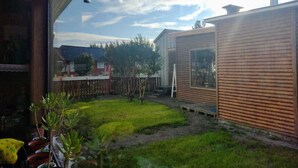 Una petita cabana de fusta amb un pati tancat per una tanca, un pont de fusta i una vista d'una casa al fons.
