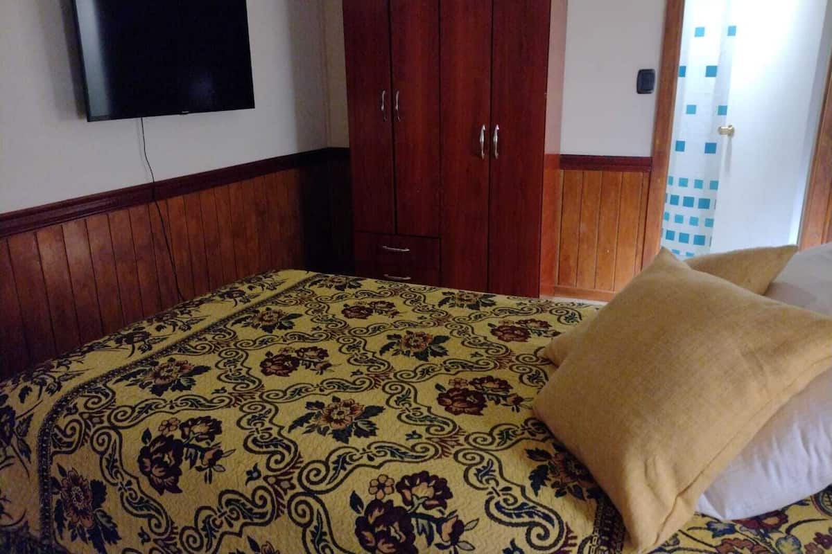 Une chambre à coucher avec un lit, une armoire en bois et un téléviseur fixé au mur.
