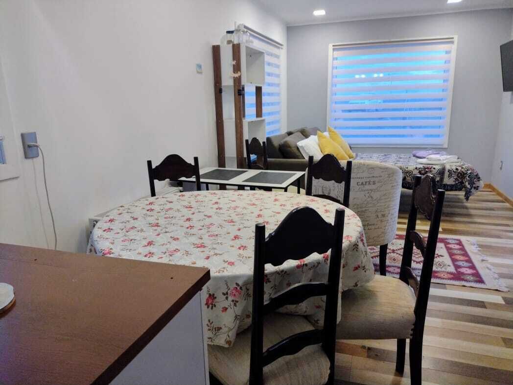 Un comedor con una mesa redonda y sillas, un sofá con funda floral y una ventana con persianas.