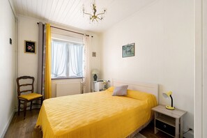 Una camera da letto con un letto, una sedia, un comodino, una lampada e una finestra con tende.