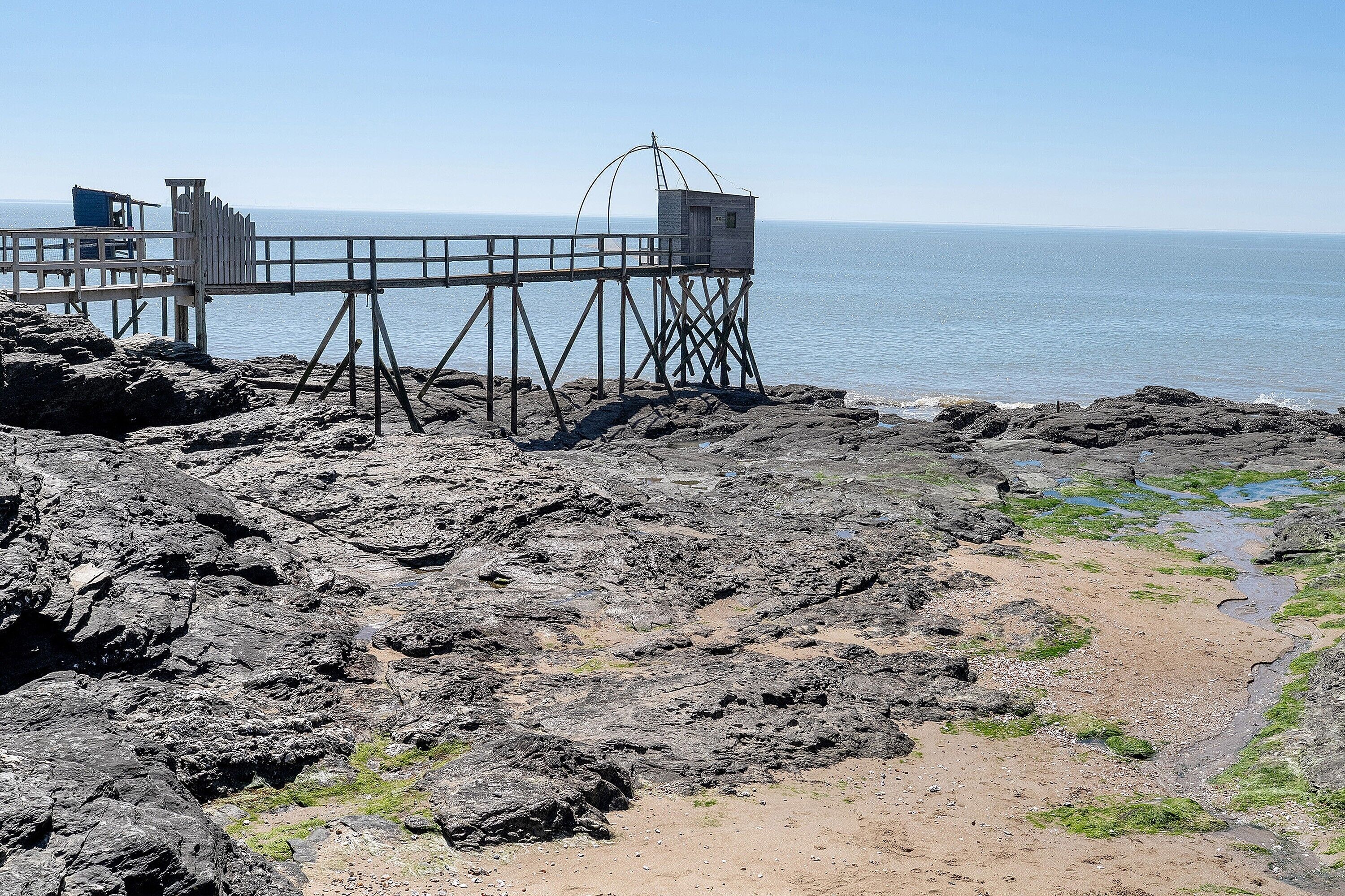 A rocky shoreline with a wooden pier extending into the water, a lifeguard tower, and a clear view of the ocean.