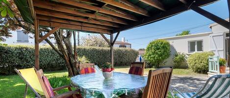 An outdoor patio with a round table, wooden chairs, and a covered area.
