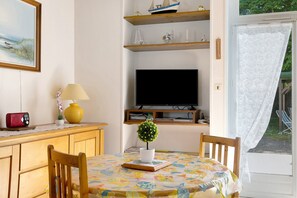 Una stanza con un tavolo in legno, sedie, una televisione, una piantina in vaso e un quadro appeso al muro.