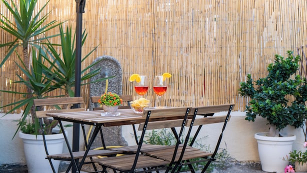 Un espacio al aire libre con mesa y bancos de madera, rodeado de plantas en macetas y una valla de bambú.