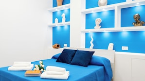 Un dormitorio moderno con colcha azul, almohadas blancas y cabecera de madera. Hay toallas blancas y un libro sobre la cama.